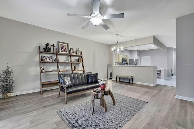 living area with light wood-style flooring, baseboards, and ceiling fan with notable chandelier