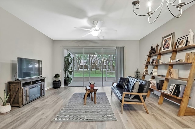 living area with ceiling fan with notable chandelier, light wood finished floors, and baseboards