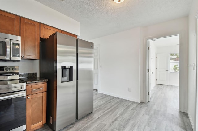 2401 Havana Dr, Clearwater, FL 33764 - kitchen with appliances with stainless steel finishes, a textured ceiling, brown cabinets, light wood finished floors, and dark stone counters