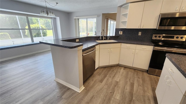 kitchen with a peninsula, light wood-style flooring, open shelves, appliances with stainless steel finishes, and a sink