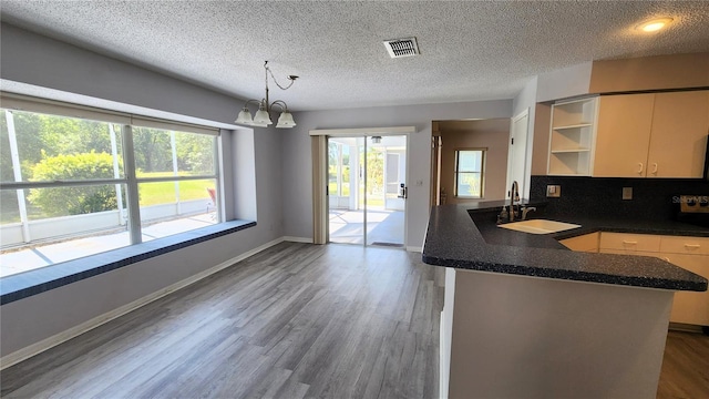 kitchen with visible vents, a sink, dark countertops, a peninsula, and wood finished floors