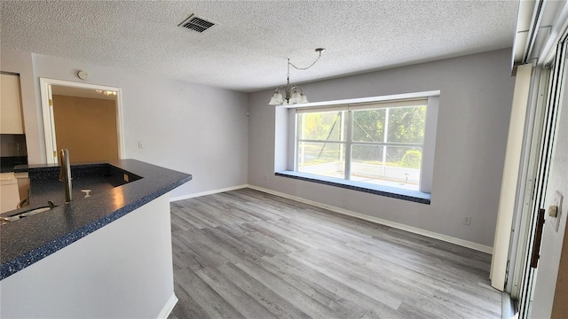 unfurnished dining area featuring a textured ceiling, visible vents, a chandelier, wood finished floors, and baseboards
