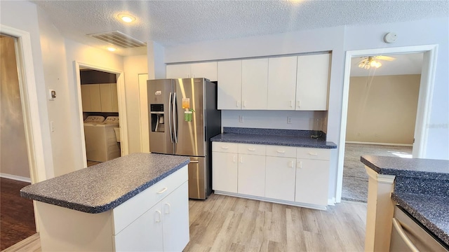 kitchen featuring light wood-type flooring, white cabinetry, washing machine and clothes dryer, dark countertops, and stainless steel appliances
