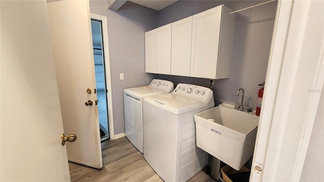 laundry room featuring light wood-style floors, washing machine and clothes dryer, a sink, baseboards, and cabinet space