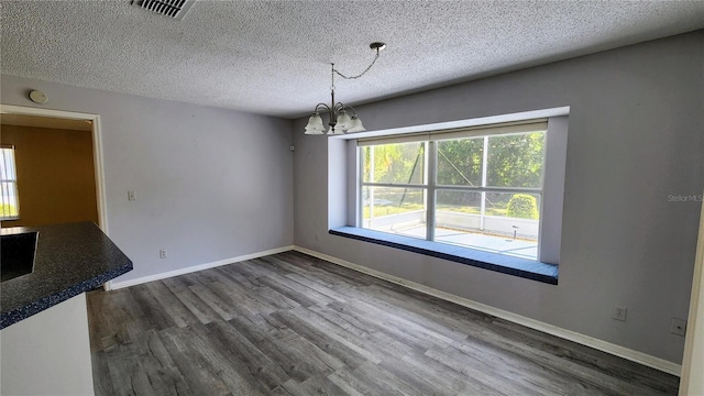 unfurnished dining area featuring baseboards, an inviting chandelier, a textured ceiling, visible vents, and dark wood finished floors