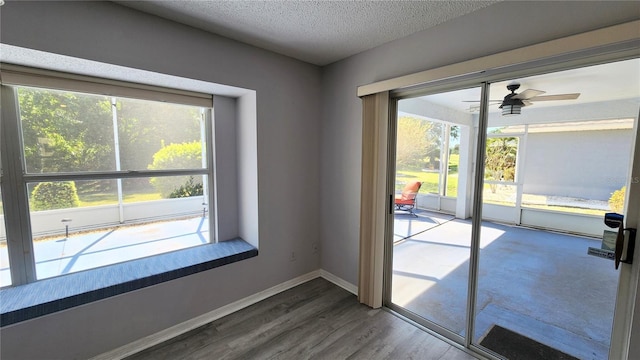 doorway to outside featuring a textured ceiling, wood finished floors, baseboards, and a ceiling fan
