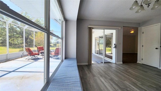 doorway with a notable chandelier, a textured ceiling, baseboards, and wood finished floors