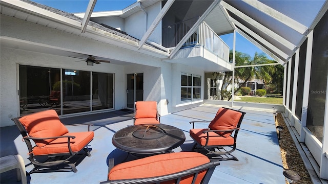 view of patio / terrace with a fire pit, a balcony, glass enclosure, and a ceiling fan