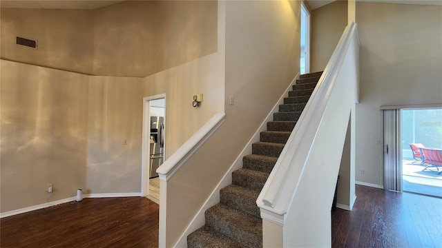 staircase with a towering ceiling, visible vents, baseboards, and wood finished floors