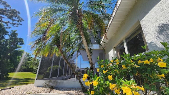 view of side of property featuring a sunroom, stucco siding, and a lawn