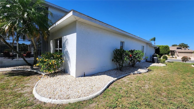 view of side of property with stucco siding, central AC unit, and a lawn