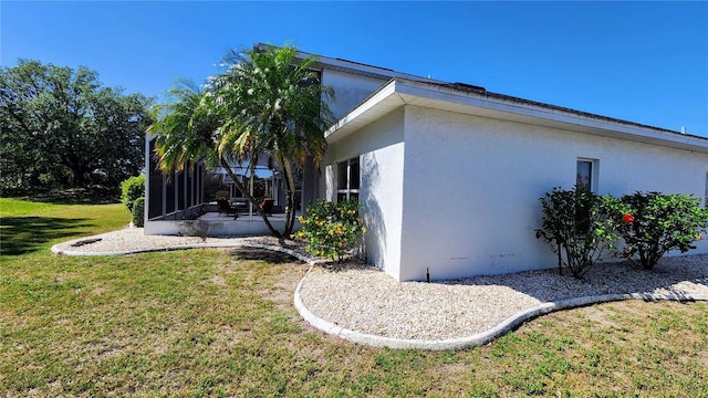 view of side of property with a yard, stucco siding, and a sunroom