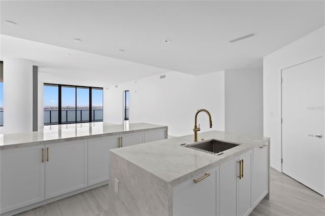 2912 W Santiago St Unit 1401, Tampa, FL 33629 - kitchen featuring a kitchen island with sink, light stone countertops, light wood-type flooring, a sink, and white cabinets