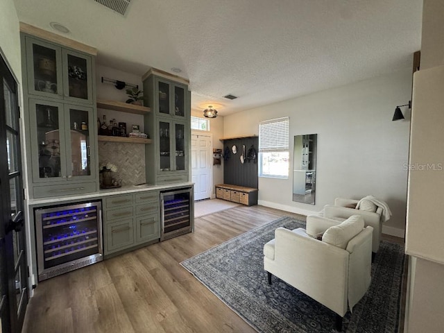 living room featuring light wood-type flooring, bar area, beverage cooler, and a textured ceiling