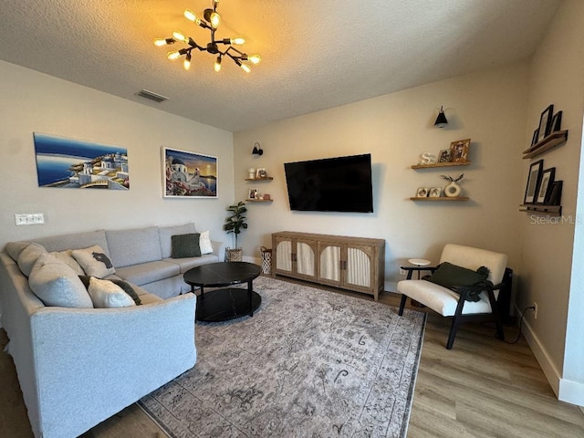 living room featuring baseboards, an inviting chandelier, a textured ceiling, light wood-style floors, and visible vents