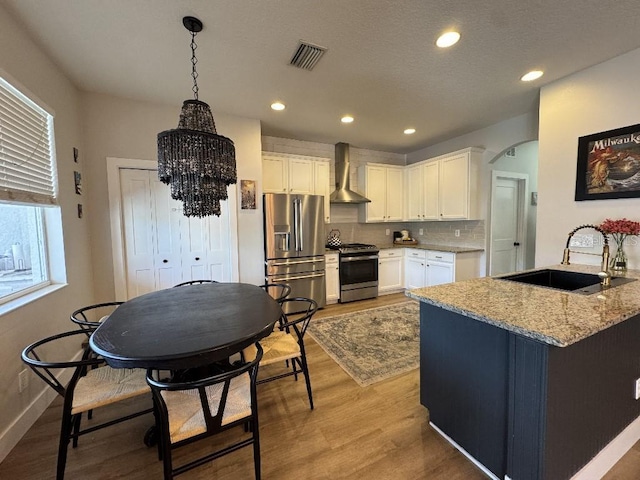 kitchen with white cabinetry, visible vents, wall chimney exhaust hood, stainless steel appliances, and a sink