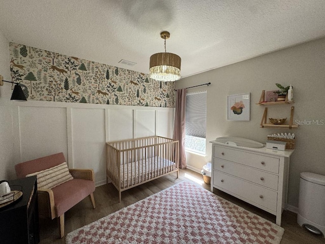 bedroom featuring a textured ceiling, visible vents, a wainscoted wall, wood finished floors, and wallpapered walls