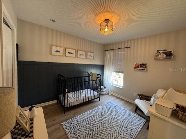 bedroom featuring wainscoting, a textured ceiling, a nursery area, and wood finished floors