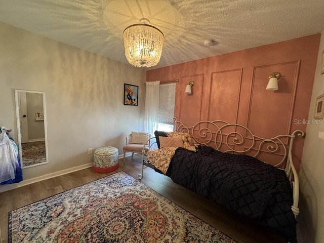 bedroom featuring a textured ceiling, wood finished floors, a notable chandelier, and baseboards
