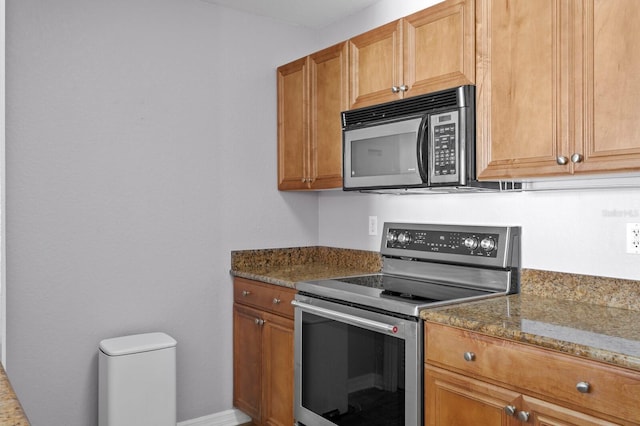 kitchen featuring stainless steel electric stove, black microwave, brown cabinetry, dark stone countertops, and baseboards