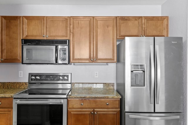 kitchen featuring stainless steel appliances, stone counters, and brown cabinetry