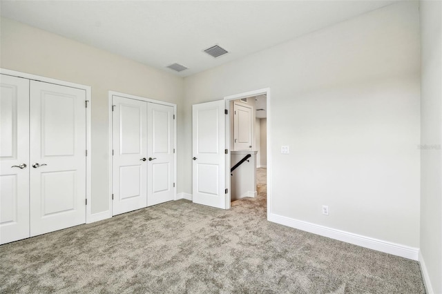 unfurnished bedroom with visible vents, baseboards, two closets, and carpet floors