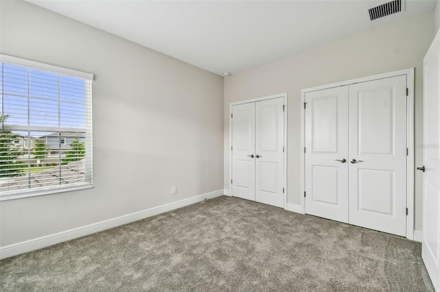 unfurnished bedroom featuring two closets, carpet flooring, baseboards, and visible vents