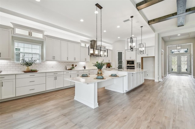 kitchen with a chandelier, a center island with sink, stainless steel microwave, and backsplash