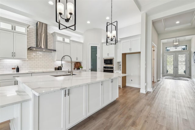 kitchen with a notable chandelier, wall chimney range hood, built in microwave, stainless steel oven, and a sink