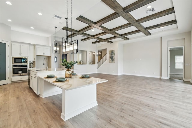 kitchen featuring light countertops, visible vents, coffered ceiling, stainless steel appliances, and a large island with sink