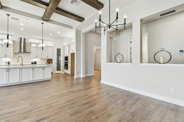 kitchen with light countertops, an inviting chandelier, wall chimney exhaust hood, and visible vents