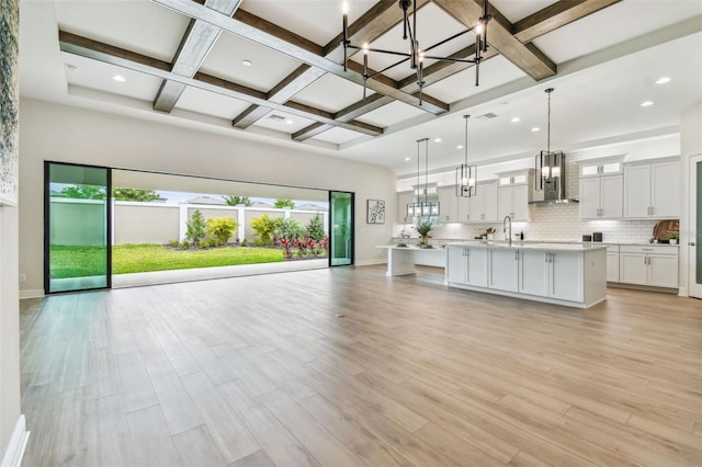 unfurnished living room with an inviting chandelier, recessed lighting, beamed ceiling, coffered ceiling, and a sink