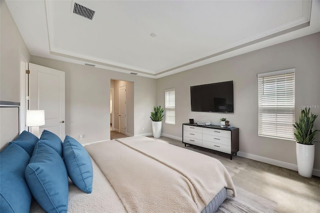bedroom with visible vents, baseboards, light colored carpet, and a raised ceiling