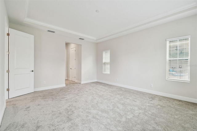 unfurnished room with light carpet, visible vents, a tray ceiling, and baseboards