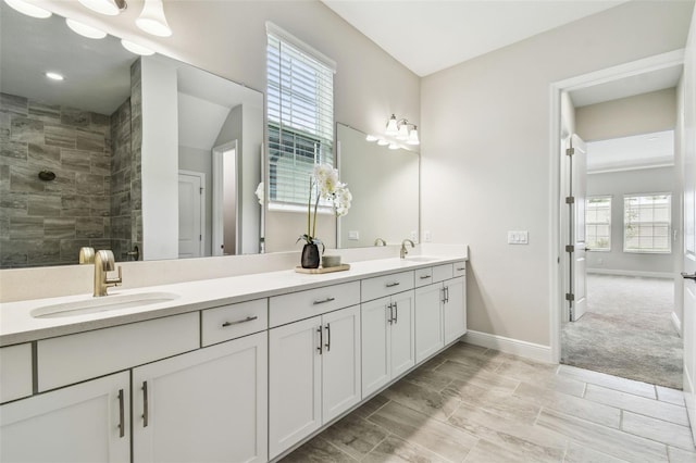 bathroom with tiled shower, double vanity, baseboards, and a sink