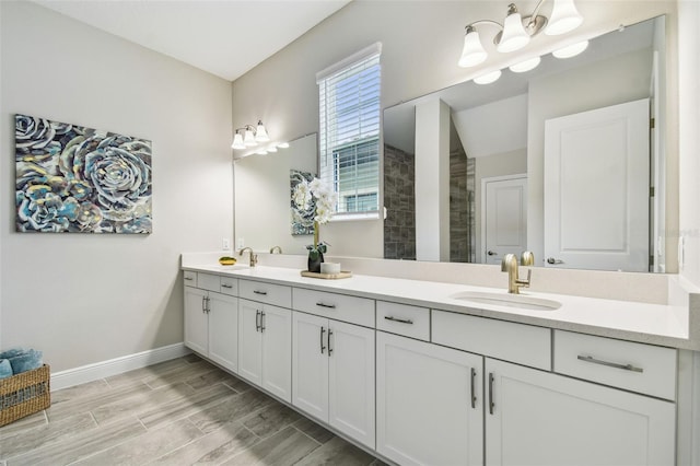 bathroom with wood finish floors, tiled shower, a sink, double vanity, and baseboards