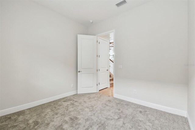 unfurnished room with visible vents, baseboards, light carpet, and stairs