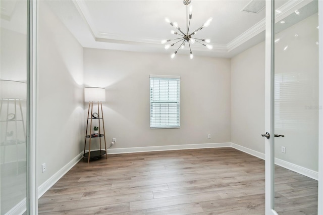 empty room with baseboards, ornamental molding, a chandelier, a tray ceiling, and light wood-style flooring