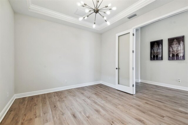 empty room featuring wood finished floors, a notable chandelier, crown molding, and a raised ceiling
