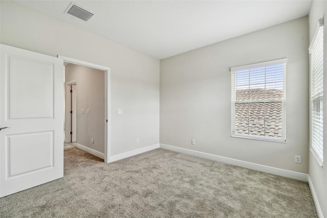 unfurnished room with a healthy amount of sunlight, light colored carpet, baseboards, and visible vents