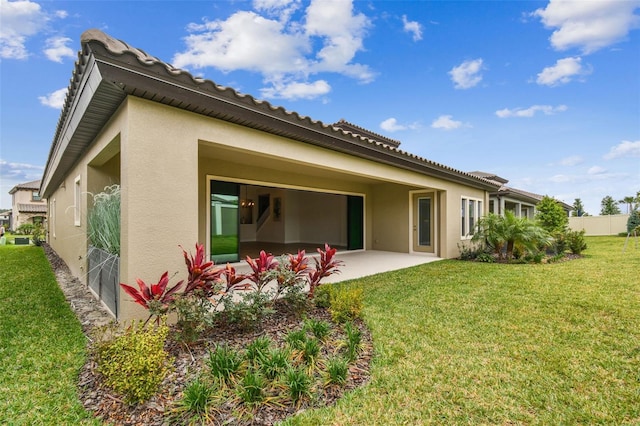 rear view of property featuring a yard, a patio area, and stucco siding
