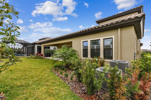 back of house with a tile roof, glass enclosure, a lawn, and stucco siding