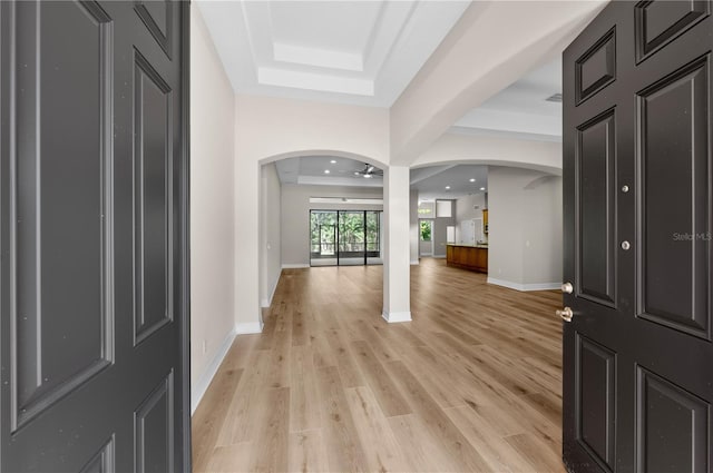 foyer entrance with baseboards, light wood-type flooring, a raised ceiling, and arched walkways