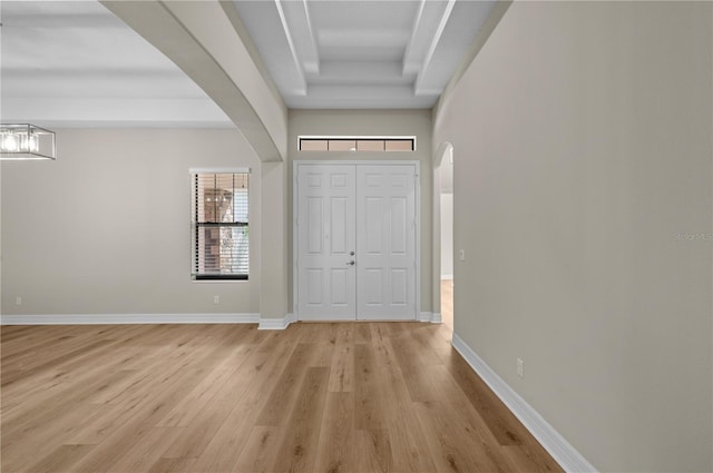 entryway with baseboards, arched walkways, light wood-style flooring, and a tray ceiling