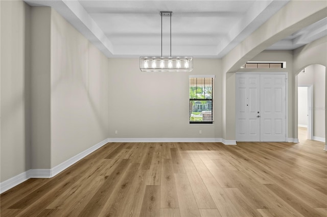 unfurnished dining area with baseboards, light wood-type flooring, a raised ceiling, and arched walkways