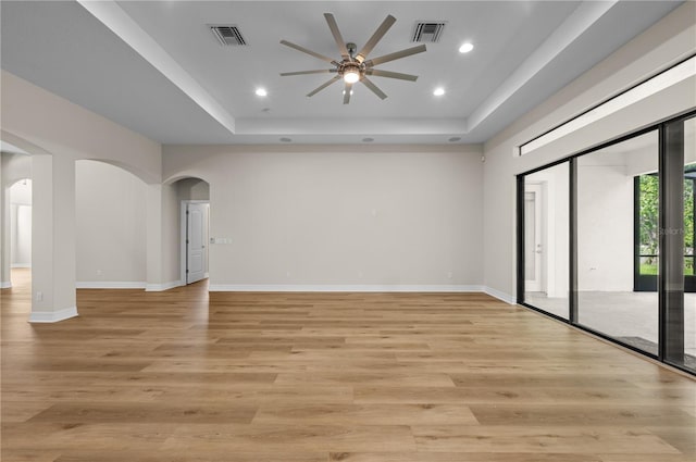 spare room with arched walkways, visible vents, a ceiling fan, and a tray ceiling