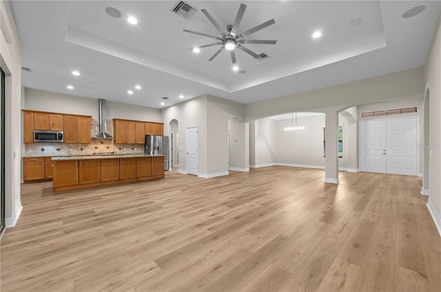 unfurnished living room featuring arched walkways, visible vents, ceiling fan, and a tray ceiling