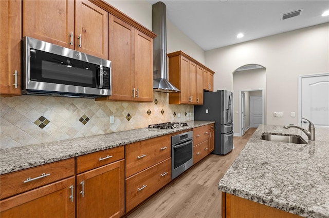 kitchen featuring light stone countertops, appliances with stainless steel finishes, a sink, visible vents, and wall chimney exhaust hood