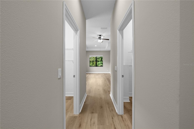hallway with a textured wall, light wood finished floors, and baseboards