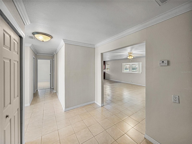 hallway featuring a textured ceiling, light tile patterned floors, baseboards, and ornamental molding
